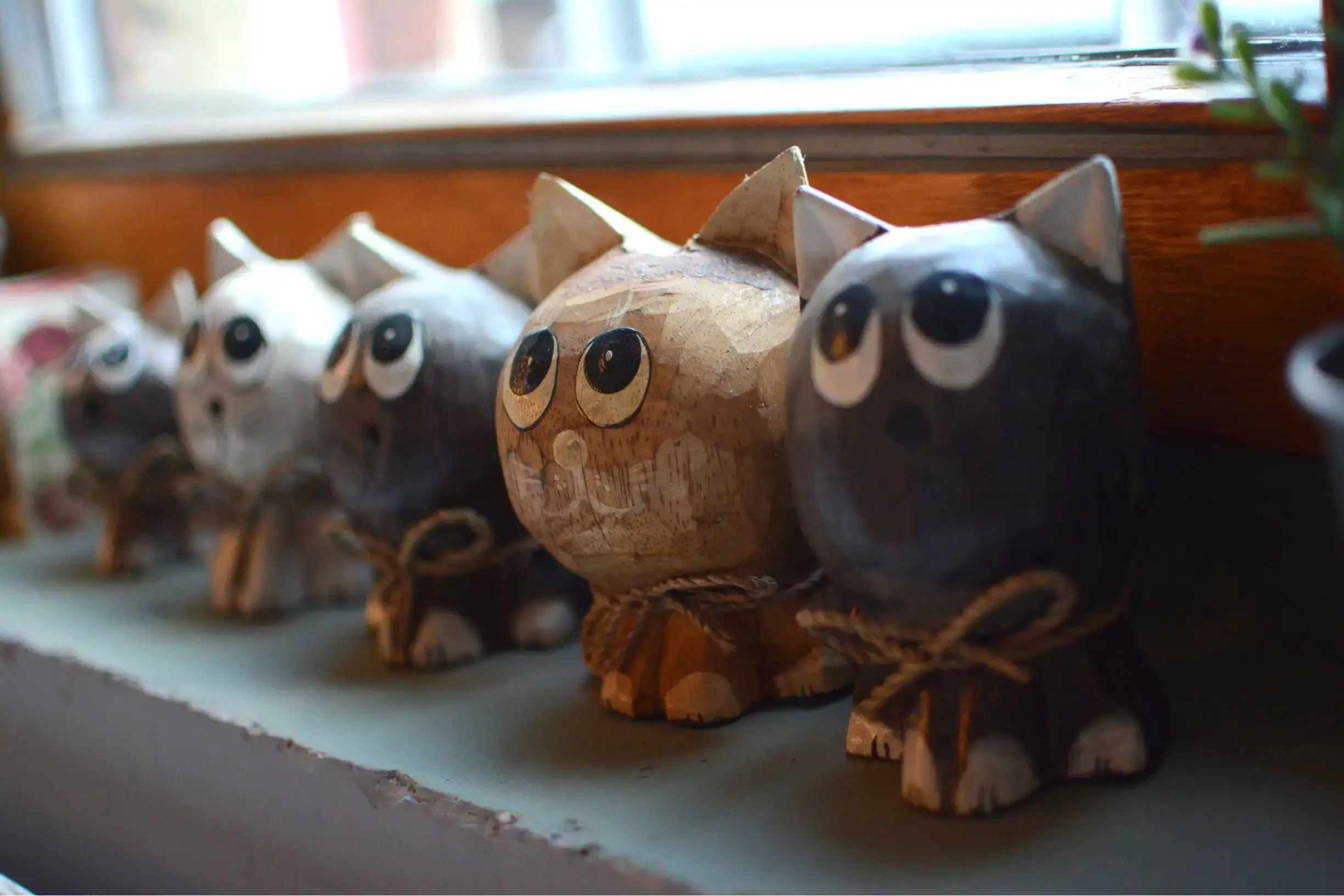 Zdjęcie przedstawia kolekcje wykonanych ręcznie z drewna kotów przypominających kolorystycznie te, które znajdują się w kawiarni.